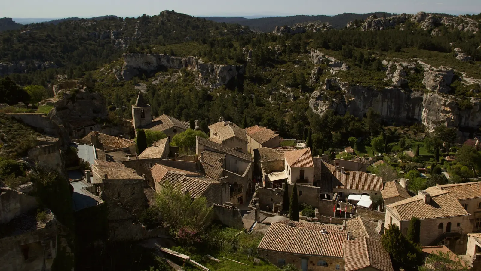 Toits de tuiles d’un village de pierre vu d’en haut, entouré de collines rocheuses et boisées
