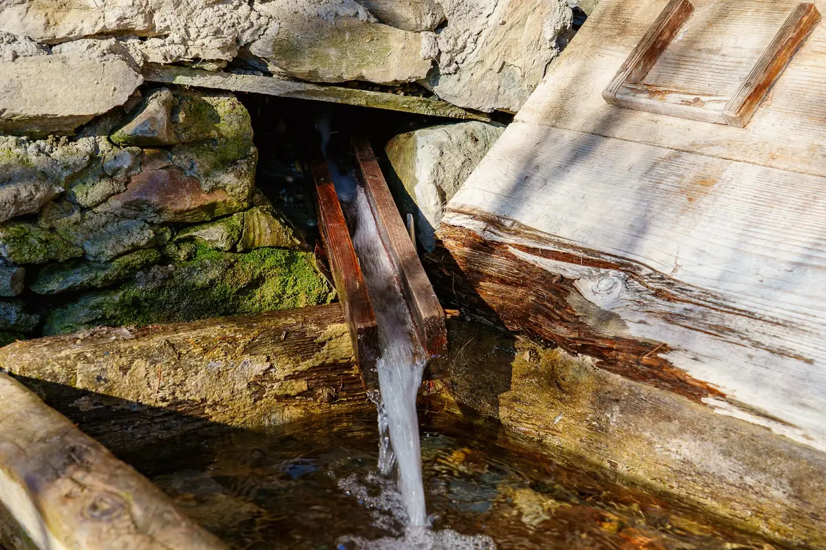 Eau qui s’écoule d’un bec en bois dans un bassin de pierre moussue