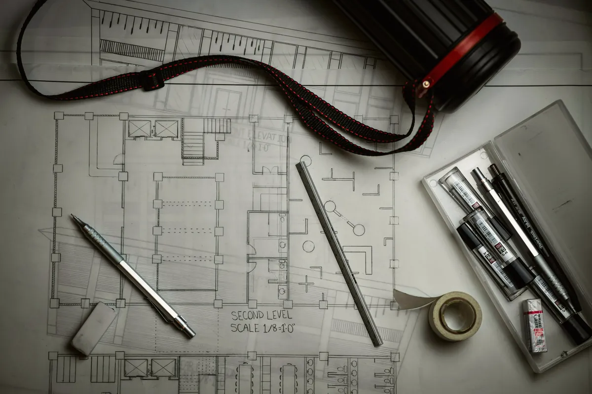 Plans d’architecte étalés sur une table avec crayons et règle métallique